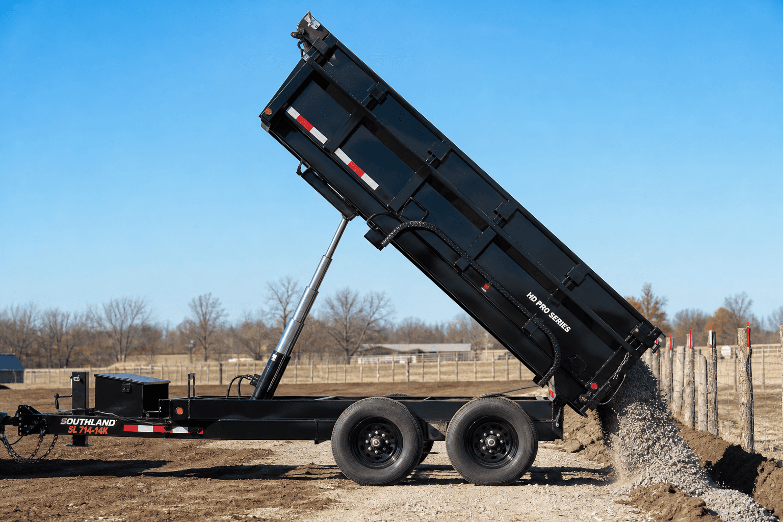Multi-stage telescopic hydraulic cylinder fully extended on dump trailer unloading gravel on fence construction jobsite